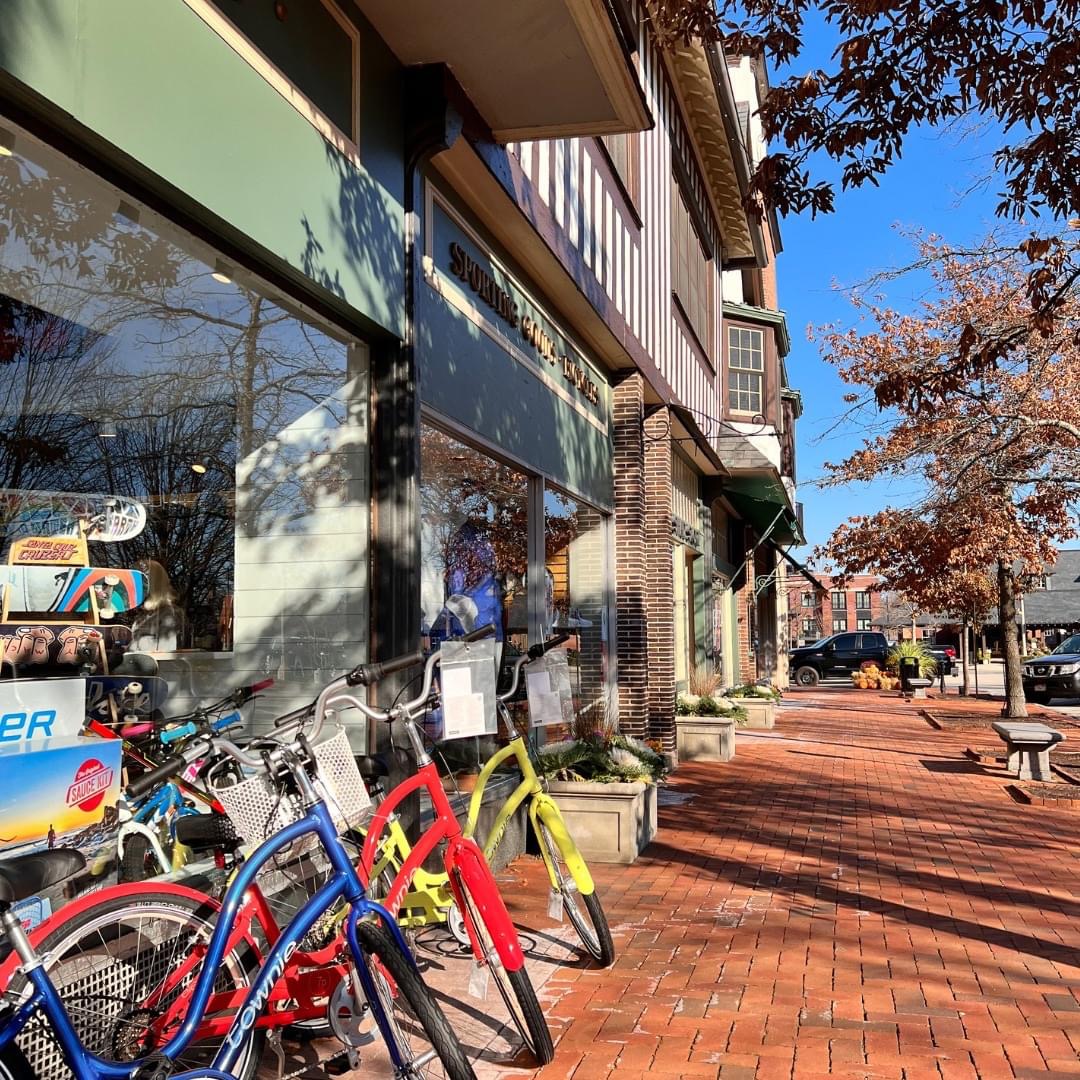 Colorful bike share bicycles parked on brick sidewalk next to urban storefronts under blue sky