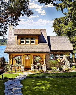 Craftsman cottage with stone foundation and wood siding beside a lake under blue sky