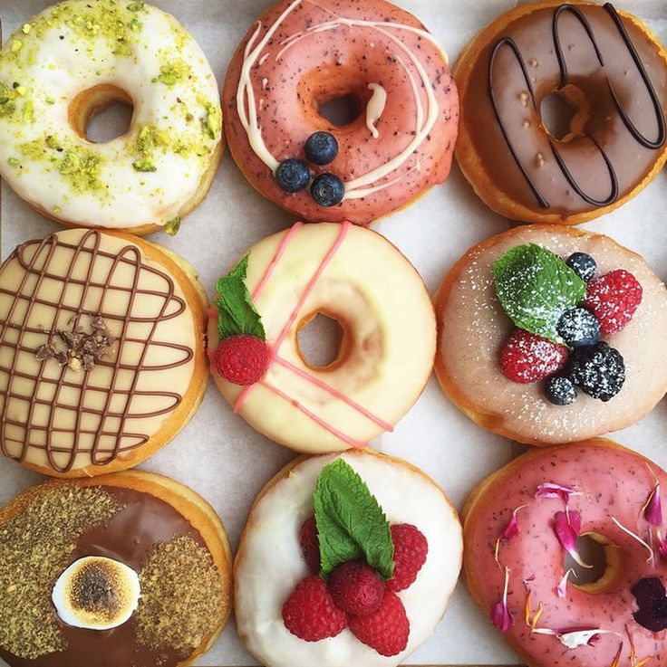 Nine decorated donuts with various toppings including berries, chocolate, and nuts arranged on white marble