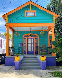Bright turquoise house with orange trim, large front porch, purple planters and yellow pots on concrete steps