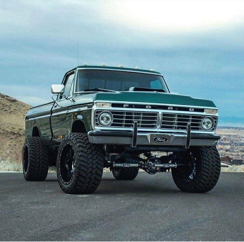 Lifted vintage pickup truck parked on a road with hills and city in the background