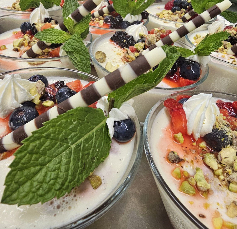 Assorted gourmet desserts with fruit skewers, puddings, berries, and mint garnish on white plates