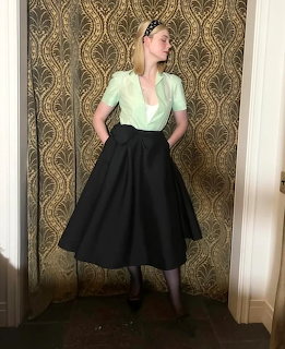 Woman in mint blouse and black skirt posing against gold damask wallpaper