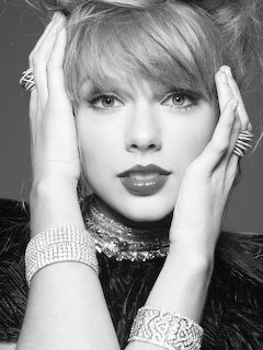 Black and white portrait of Taylor Swift with hands near face, wearing statement jewelry and feathered accessories