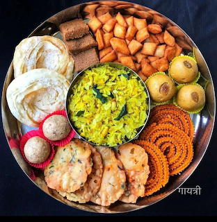 Circular metal platter with assorted Indian snacks including poha, namkeen, flatbreads, and fried items