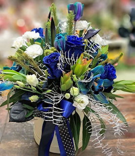 Elegant blue and white flower bouquet with roses, lisianthus, and peacock feathers in a white box