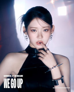 Young woman with dark hair in ponytail wearing black outfit and silver rings posing with hand near face