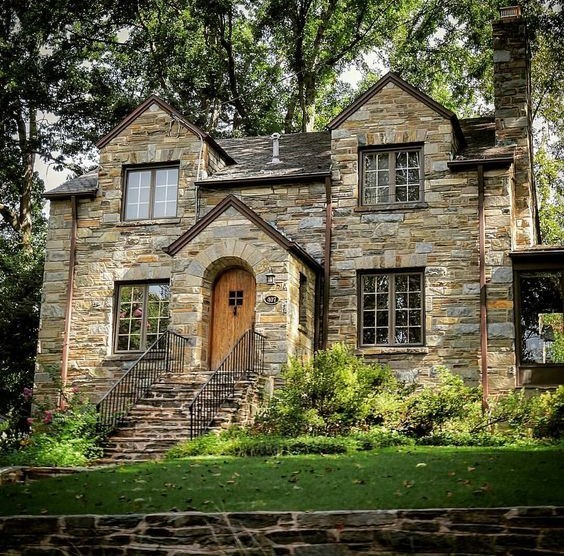 Stone cottage house with arched wooden door, stone steps, and surrounding green trees