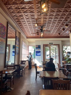 Cafe interior with ornate tin ceiling, wooden furniture, pendant lights, and large windows