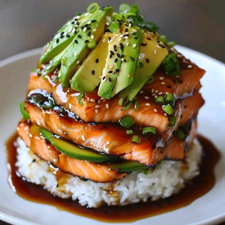 Stacked salmon and rice dish topped with avocado, pineapple, sesame seeds, and sauce