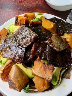 White plate with salad containing roasted sweet potato, avocado, seaweed chips, spring rolls, and grens