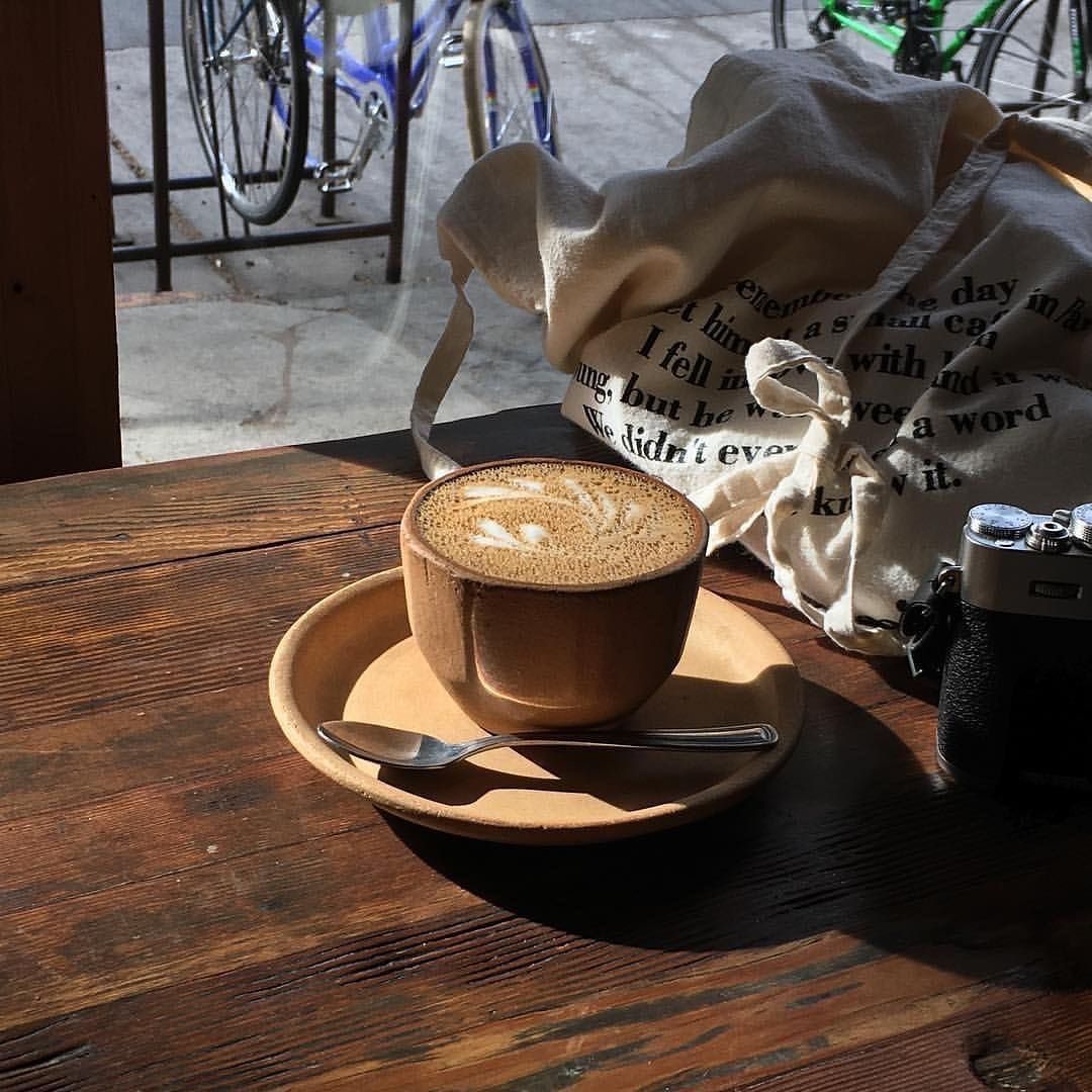Cappuccino with latte art on a saucer and spoon on a wooden table by a window