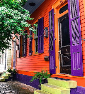 Bright orange house with purple shutters, door, and colorful planters on sidewalk with green plants