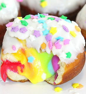 Donut with white frosting, colorful sprinkles, and rainbow filling dripping out