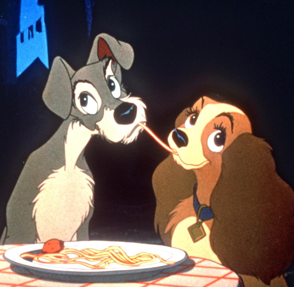 Cartoon dogs Lady and Tramp sharing a strand of spaghetti at a dinner table