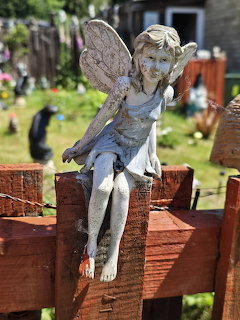 Weathered gray fairy statue with wings sitting on wooden fence in garden setting