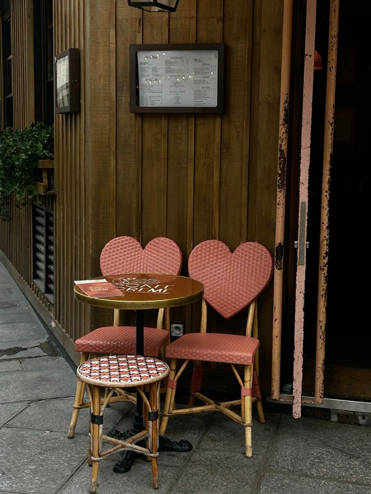 Two red heart-shaped bistro chairs and a round table outside a Paris café with wooden walls