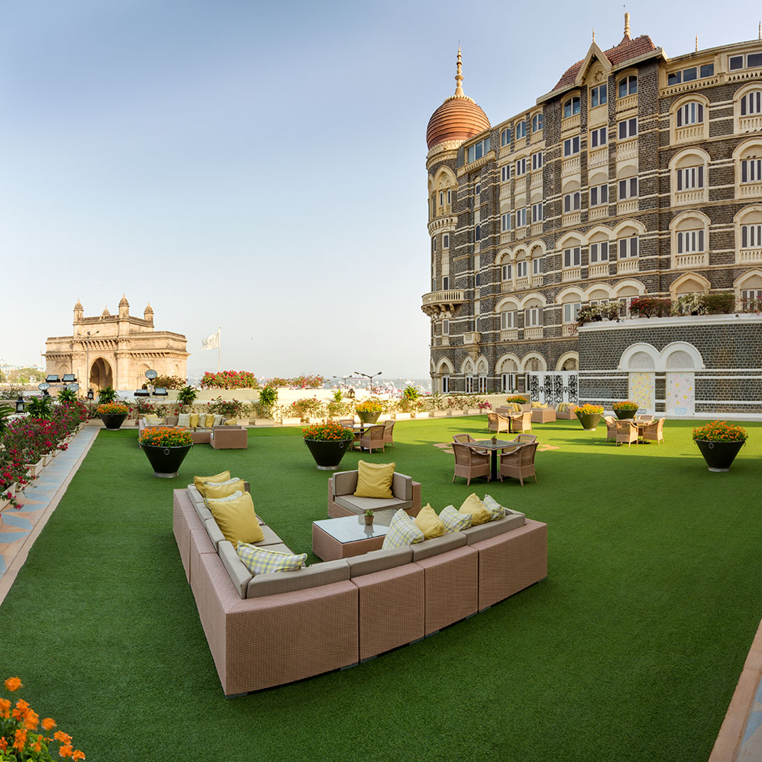 Roftop terrace with sofas and green lawn facing Gateway of India and Taj Mahal Palace Hotel