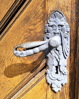 Ornate silver metal door handle shaped like a bearded face on a wooden door