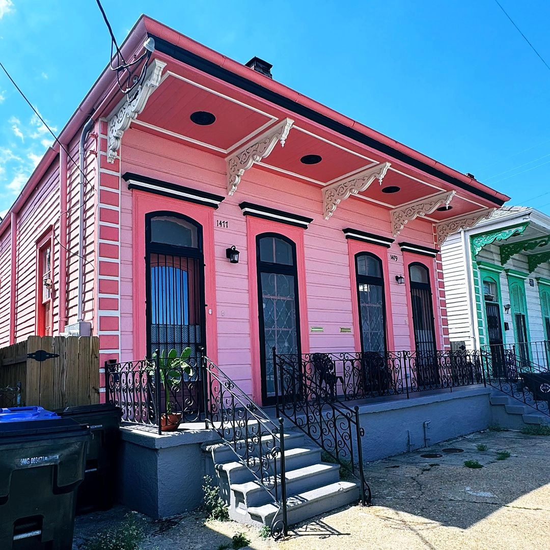 Bright pink historic house with white ornamental trim, black shutters, front porch steps with iron railings