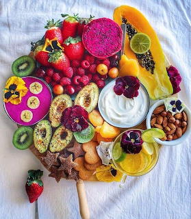 Colorful fruit platter with strawberries, kiwi, dragon fruit, yogurt, almonds, and edible flowers