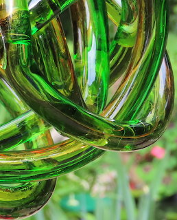 Close-up of a green glass decorative ball made of intertwined tubular loops with light reflections