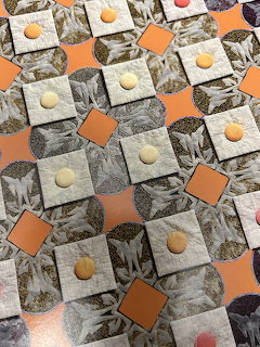 Patchwork quilt with grayscale squares, orange pieces, and small round buttons