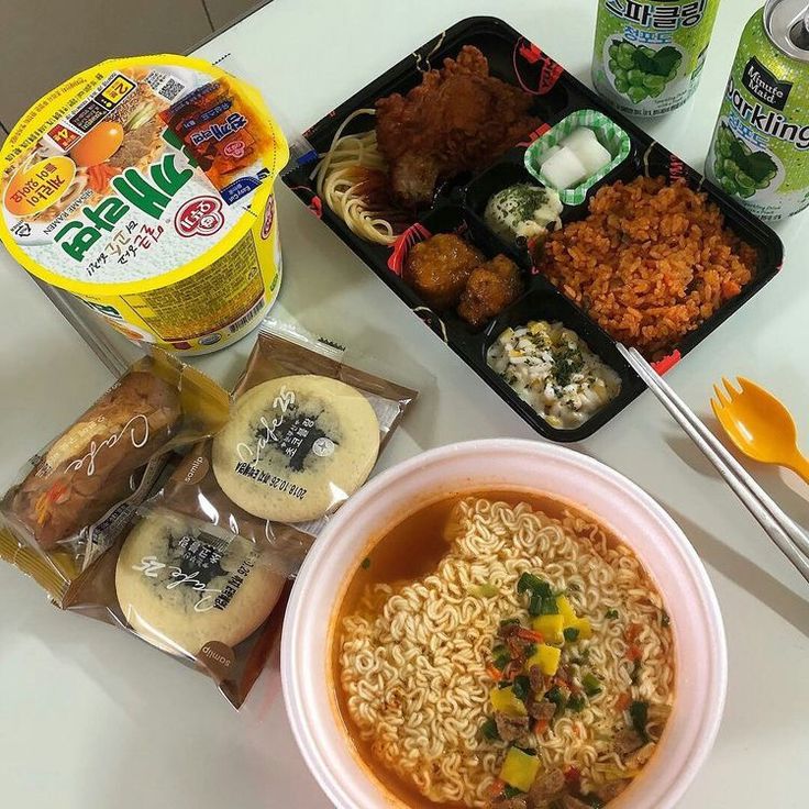 Korean meal with instant ramen, bento box of fried items and rice, bread rolls, and drinks on a table