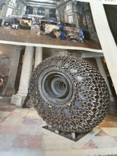 Industrial tire sculpture constructed from interwoven steel chains and metal rings on tiled floor