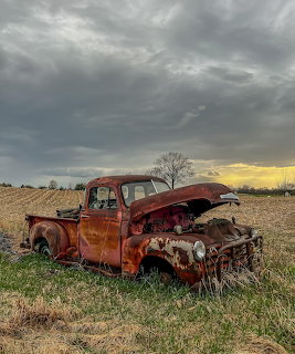 Rusty abandoned 1953 Chevy pickup truck in a farm field under stormy skies at sunset