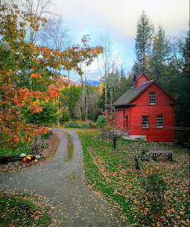 Red wooden building beside a gravel path surrounded by colorful fall foliage in Vermont