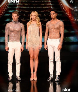 Three models in glittery sheer outfits posing on a dark fashion show stage