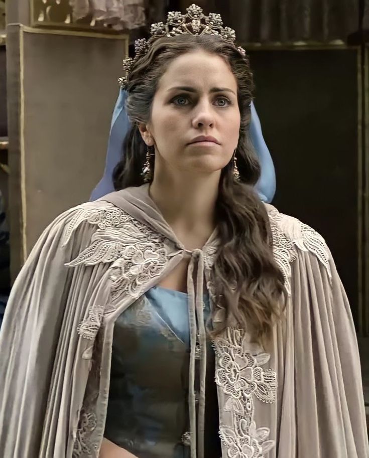 Young woman in royal costume with silver tiara, blue headscarf, and lace-trimmed cape