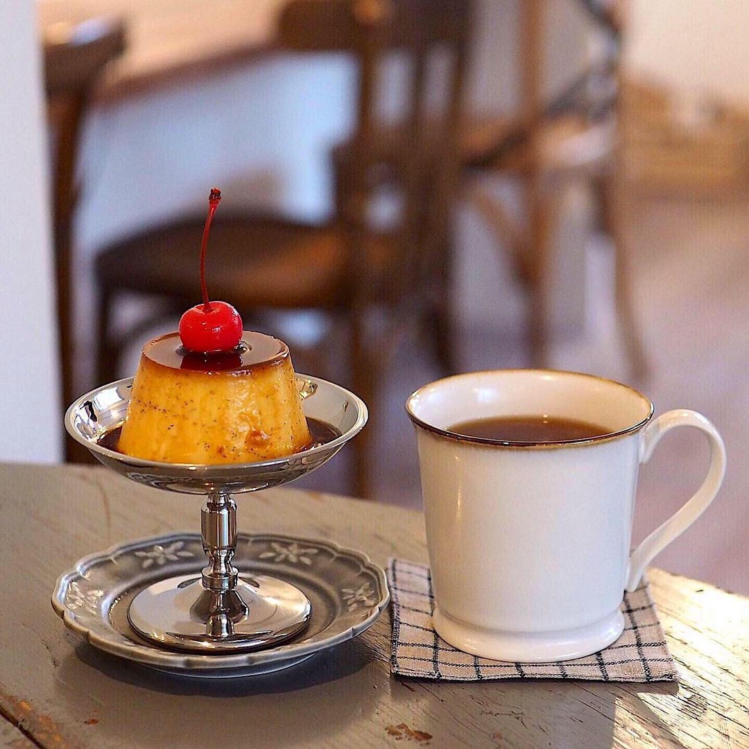 Black coffee beside a custard pudding with a cherry on a cafe table