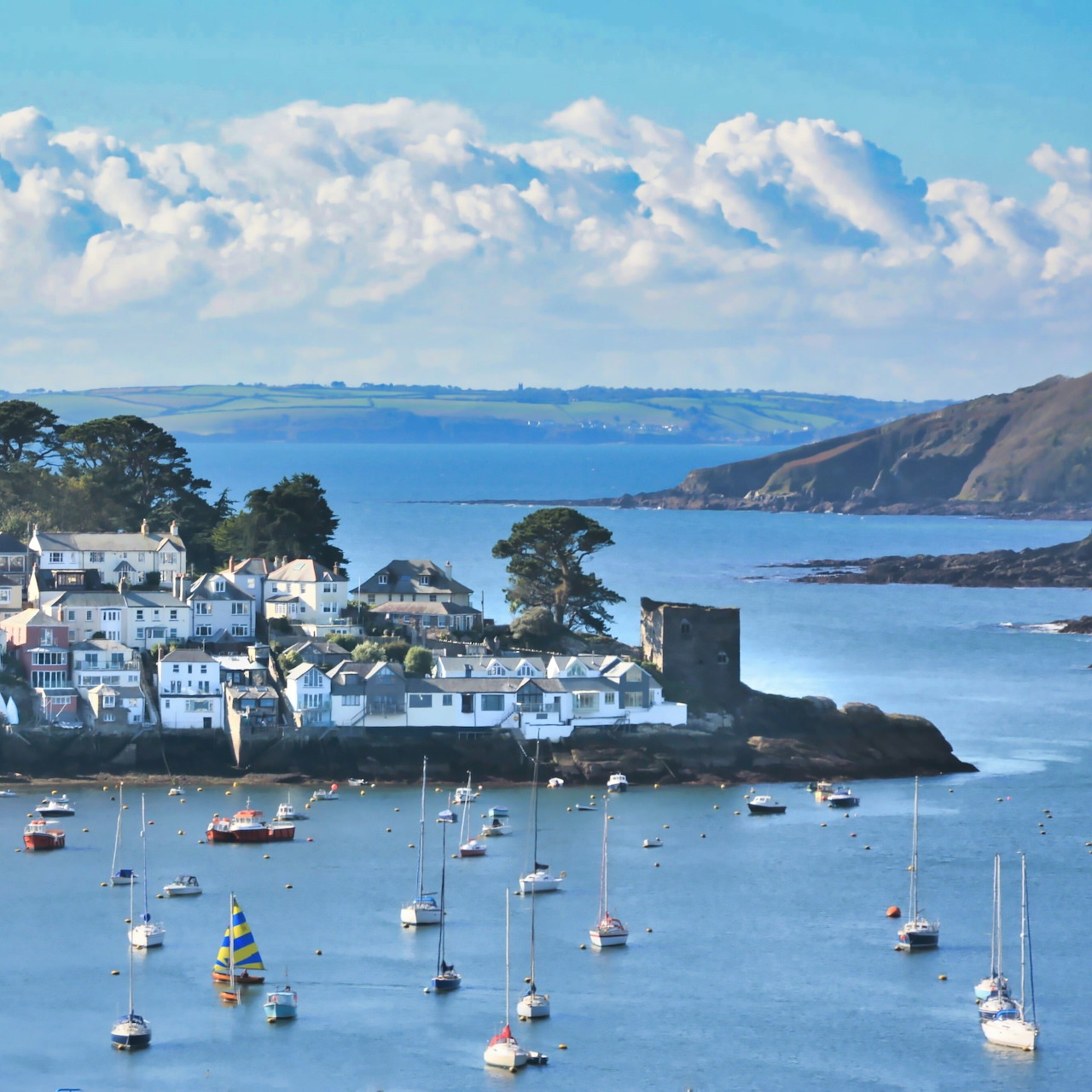 Coastal village with white houses and sailboats in a calm blue harbor under a cloudy sky