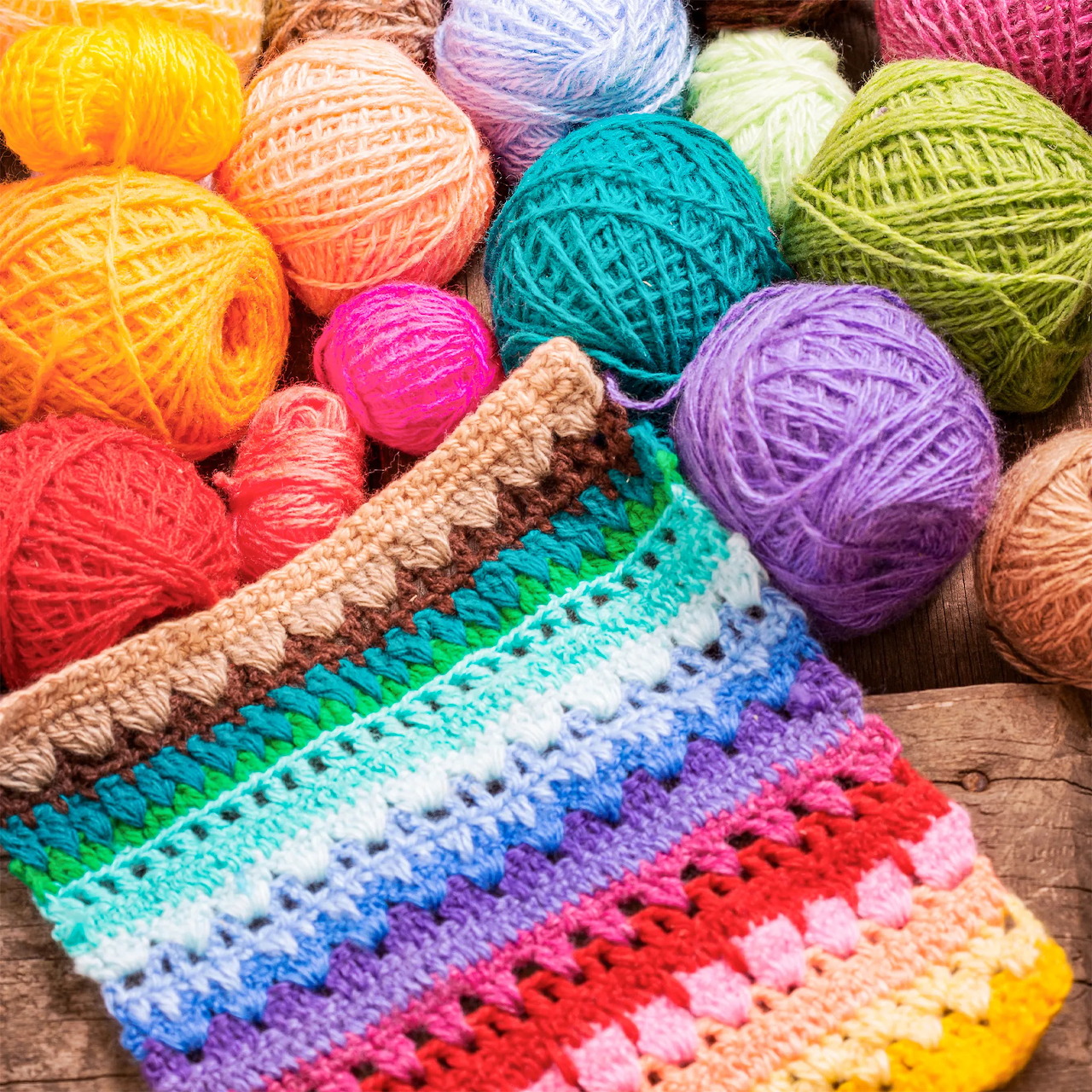 Assorted colorful yarn balls with rainbow crochet work on wood