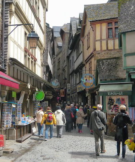 Tourists walking down a narrow medieval street with traditional half-timbered buildings and shops at Mont Saint-Michel