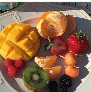 Assorted fresh fruits arranged on a white plate with mango, berries, kiwi, and citrus