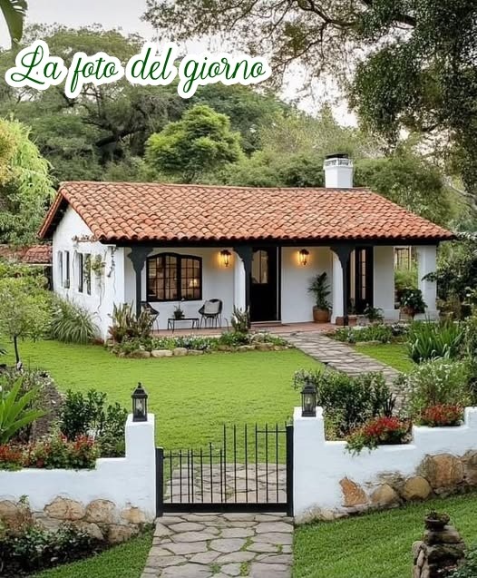 White cottage with red tile roof, front gate, green lawn, and garden trees
