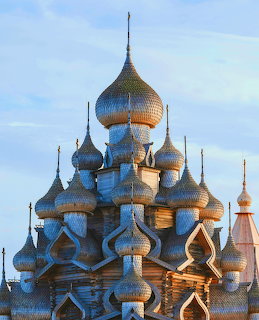 Historic wooden church with many onion domes under a pale blue sky