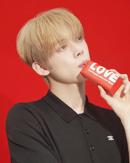 Blonde young man in black polo drinking from red LOVE juice box against red background
