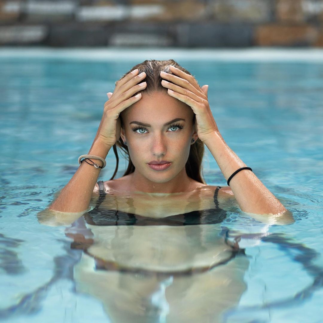 Woman with wet hair in swimming pool looking at camera