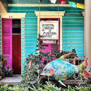 Colorful turquoise building with pink shutters and large decorative fish sculpture on porch