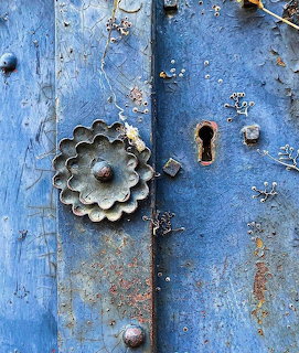 Close-up of weathered blue door with ornate brass keyhole and decorative metal hardware