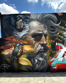 Street art mural of a bearded man with flowing hair, a bird, and colorful graffiti on a wall
