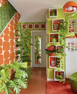 1970s retro room with orange patterned wall, green shelves, and many houseplants