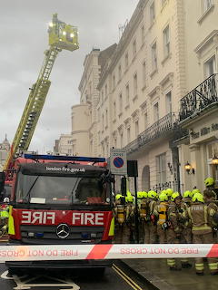 London fire engine with aerial ladder extended outside a Paddington hotel, firefighters in yellow gear on scene
