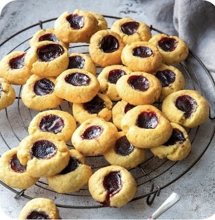 Golden thumbprint cookies with dark jam centers cooling on wire rack