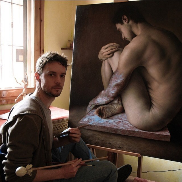 Male artist in studio sitting beside a large realistic painting of a nude male figure