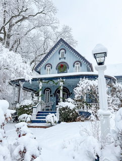 Snow-covered blue house with frosted trees, shrubs, and a white lamp post in winter